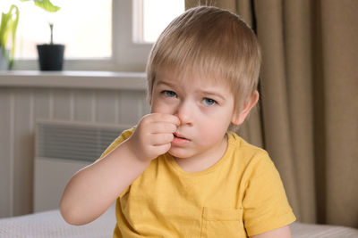 Child boy with blonde hair baby with finger in his nose. portrait 3 years old kid picking his nose.