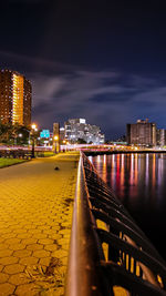 Illuminated buildings by street against sky at night