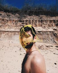 Portrait of shirtless young man with torn net on face standing on beach