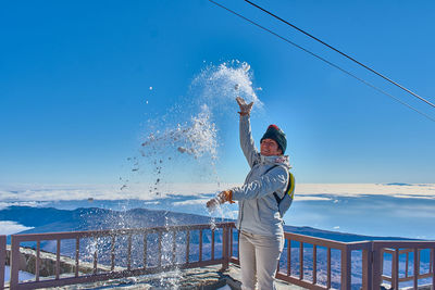 Side view of woman playing with snow on snowcapped mountain