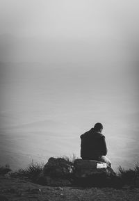 Rear view of silhouette woman sitting by sea against clear sky