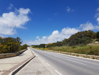 Empty road by trees against blue sky