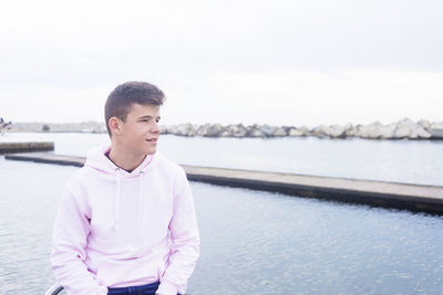 Young man looking away while sitting against sky