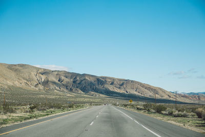 Empty road by mountains against clear sky