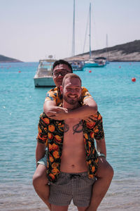 Portrait of happy homosexual couple at beach against clear sky