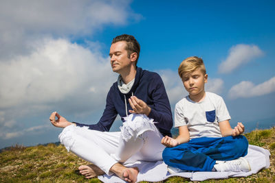 Small boy and his father practicing yoga and meditating with eyes closed in nature. copy space.