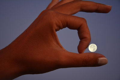 Optical illusion of large hand by moon against sky at night