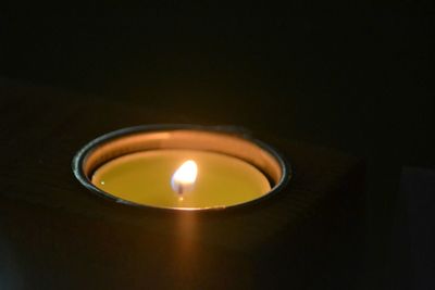 Close-up of illuminated tea light candle in darkroom