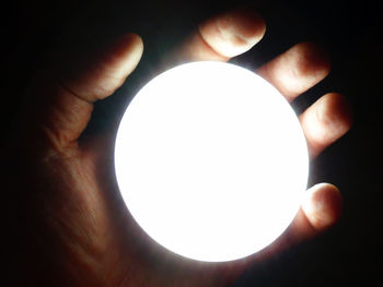 Close-up of hand holding illuminated lamp against black background