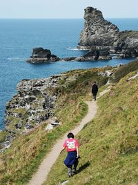 Rear view of boys walking on mountain by sea