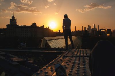 Silhouette of man standing in city against sky during sunset