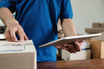 Midsection of delivery man using digital tablet by box at table