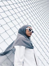Woman wearing sunglasses and hijab while standing against wall