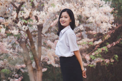 Portrait of smiling young woman standing against trees