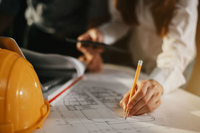 Midsection of woman drawing blueprint on table