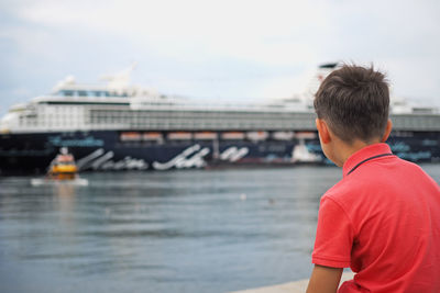 Rear view of boy looking at ship sailing in sea against sky