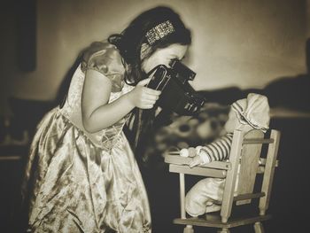 Side view of girl photographing doll on chair at home