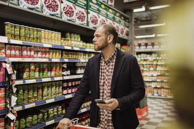 Male customer holding smart phone while shopping in grocery store