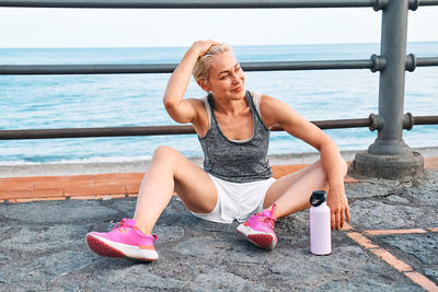 Fit woman relaxes on seaside promenade after running and training on a road by the sea.