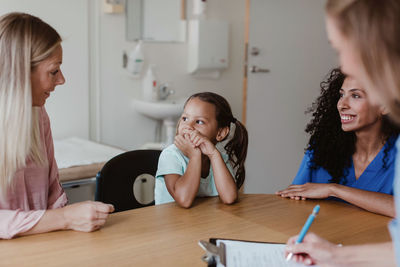 Mother talking to girl while healthcare workers looking at them in medical examination room