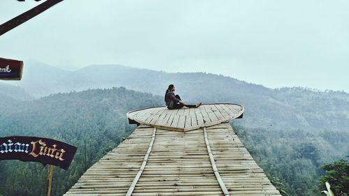 Side view of woman sitting on wood against sky