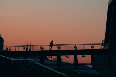 Silhouette man walking on bridge against sky during sunset