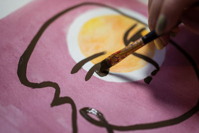 Closeup view of crop unrecognizable female artist creating picture with paint and brush on canvas in workshop