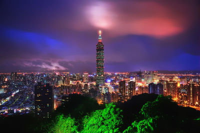 Illuminated buildings against cloudy sky at night