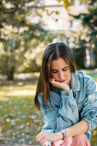 Worried woman with hand on chin sitting at park