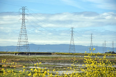 Electricity pylon on field against cloudy sky