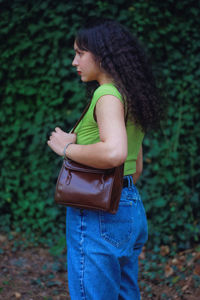Side view of woman standing on field holding a purse/bag