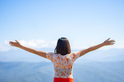 Rear view of woman with arms outstretched standing against sky