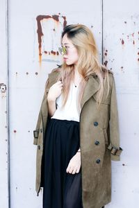 Young woman in long coat standing against wall