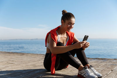 Young woman using mobile phone at beach against sky