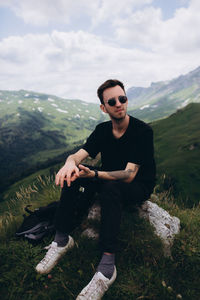 Full length of man sitting on mountain against sky