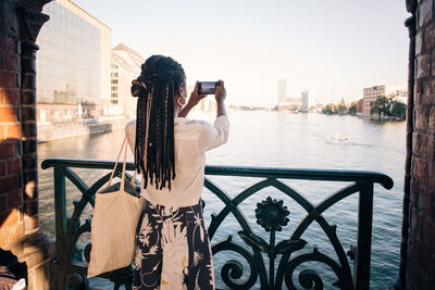 Rear view of young woman photographing river in city