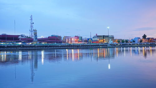 River by illuminated city against sky at dusk