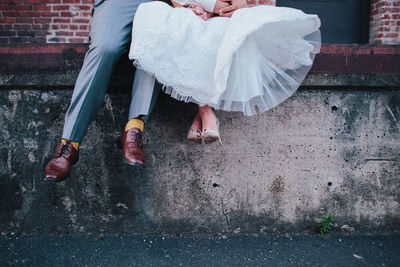 Low section of wedding couple sitting on retaining wall