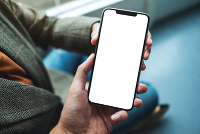 A woman holding and showing white mobile phone with blank black desktop screen to someone