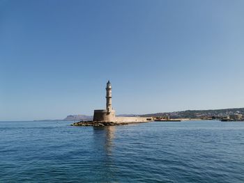 Lighthouse by sea against clear sky