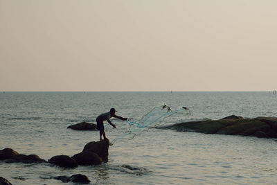 Fisherman throwing net on sea against sky