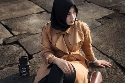 Muslim tourist woman wearing hijab / headscarf and brown coat at ratu boko temple, yogyakarta