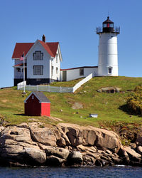 Lighthouse amidst rocks and buildings against sky