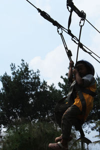 Low angle view of boy climbing on tree against sky