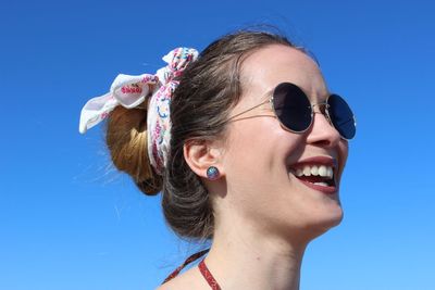 Smiling woman wearing sunglasses against clear blue sky