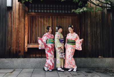 Portrait of smiling friends wearing traditional clothing against wall