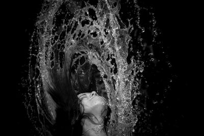 Portrait of woman splashing water against black background