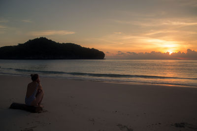 Woman sitting on beach against sky during sunset