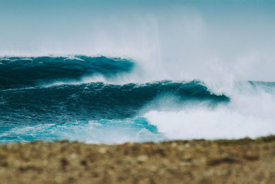 Scenic view of waves breaking on beach against sky