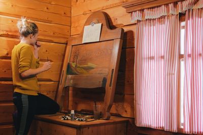 Woman drawing on canvas while standing in cottage